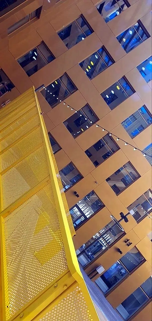 Perforated yellow balustrade against a facade of windows