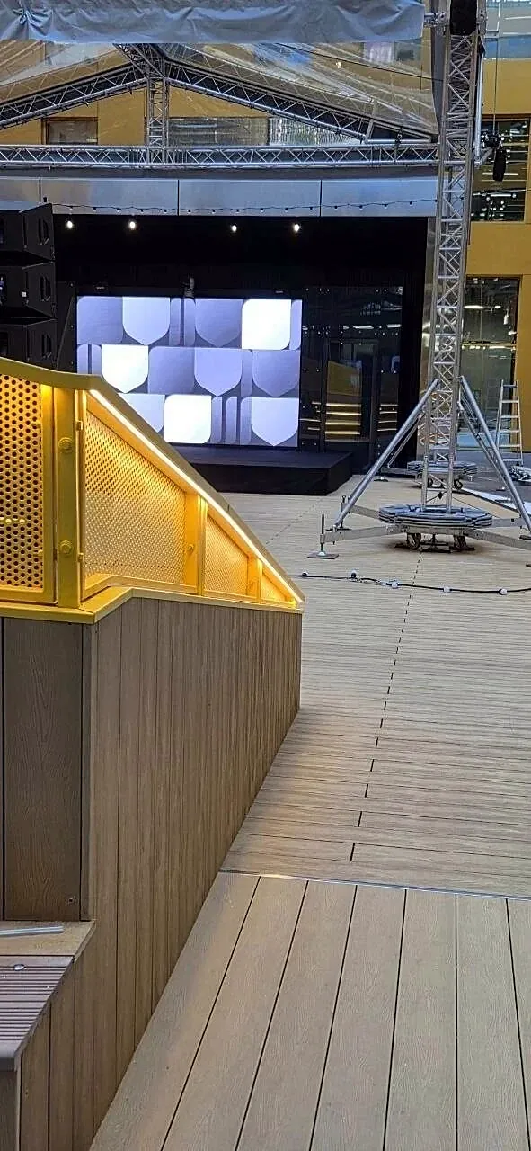 Timber walkway with a yellow perforated balustrade leading to a stage