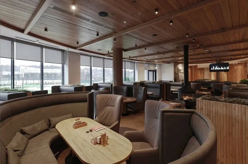 Restaurant hall with curved booth sofas, a timber ceiling and a hanging fireplace