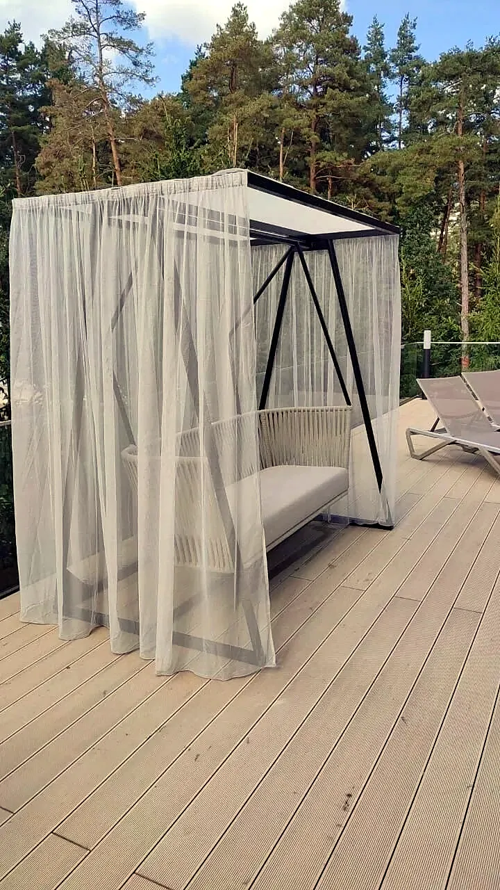 Garden swing with a steel frame and sheer curtains on a timber terrace