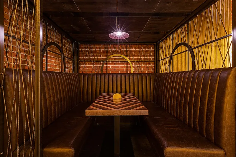 Leather booth with a timber table between brick walls and metal arches