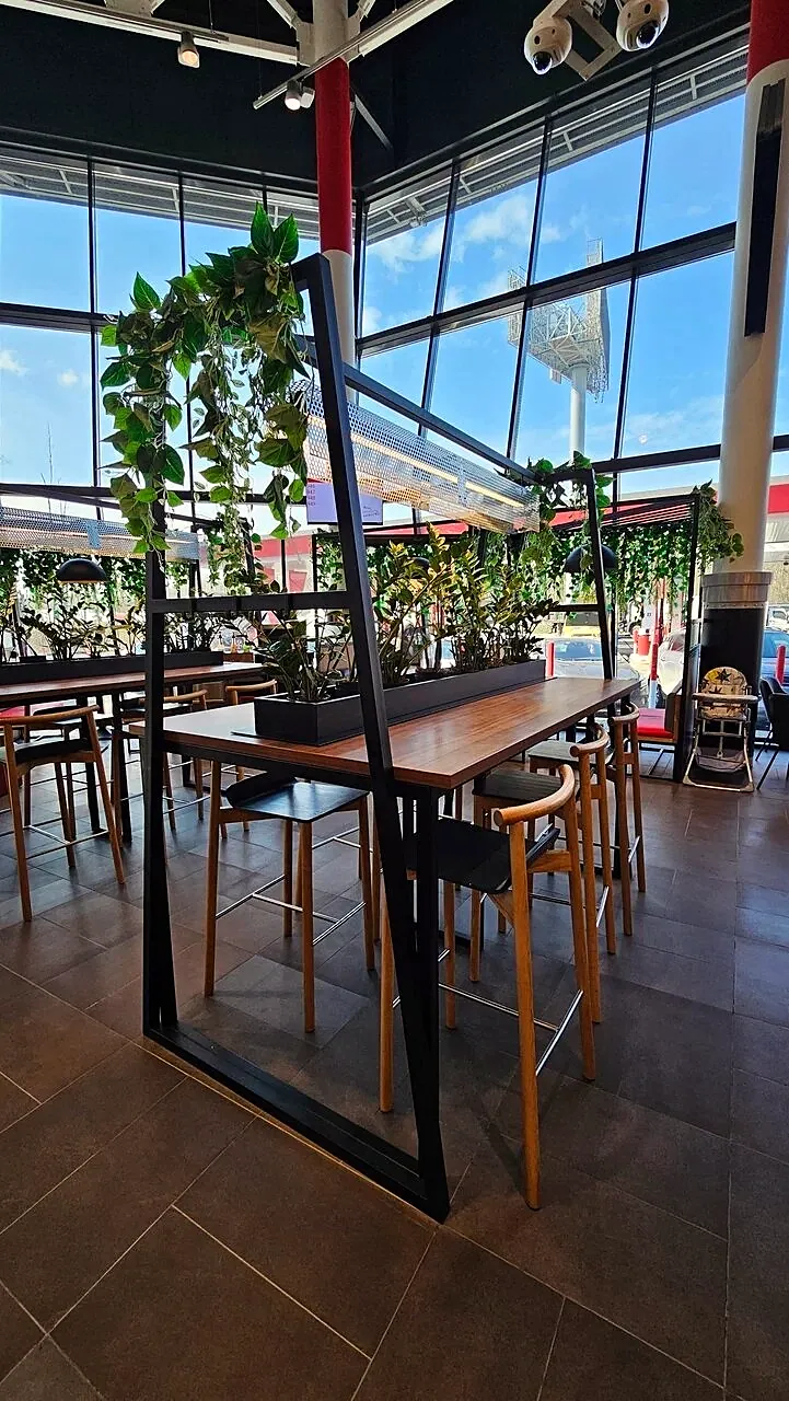 Bar tables on black steel frames under a planted partition
