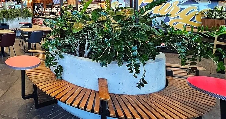 Round bench with timber slats around a large concrete planter, with red-topped tables