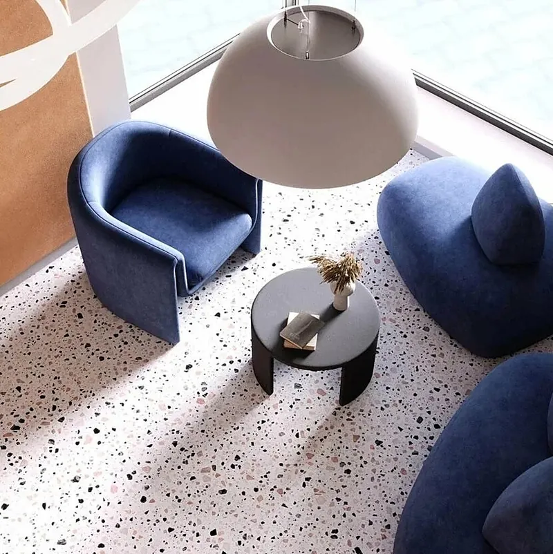 Two navy armchairs and a round table on a terrazzo floor