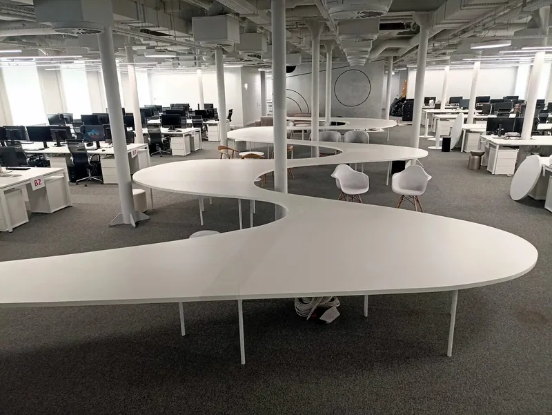 Long curving white communal table on thin supports in an open office